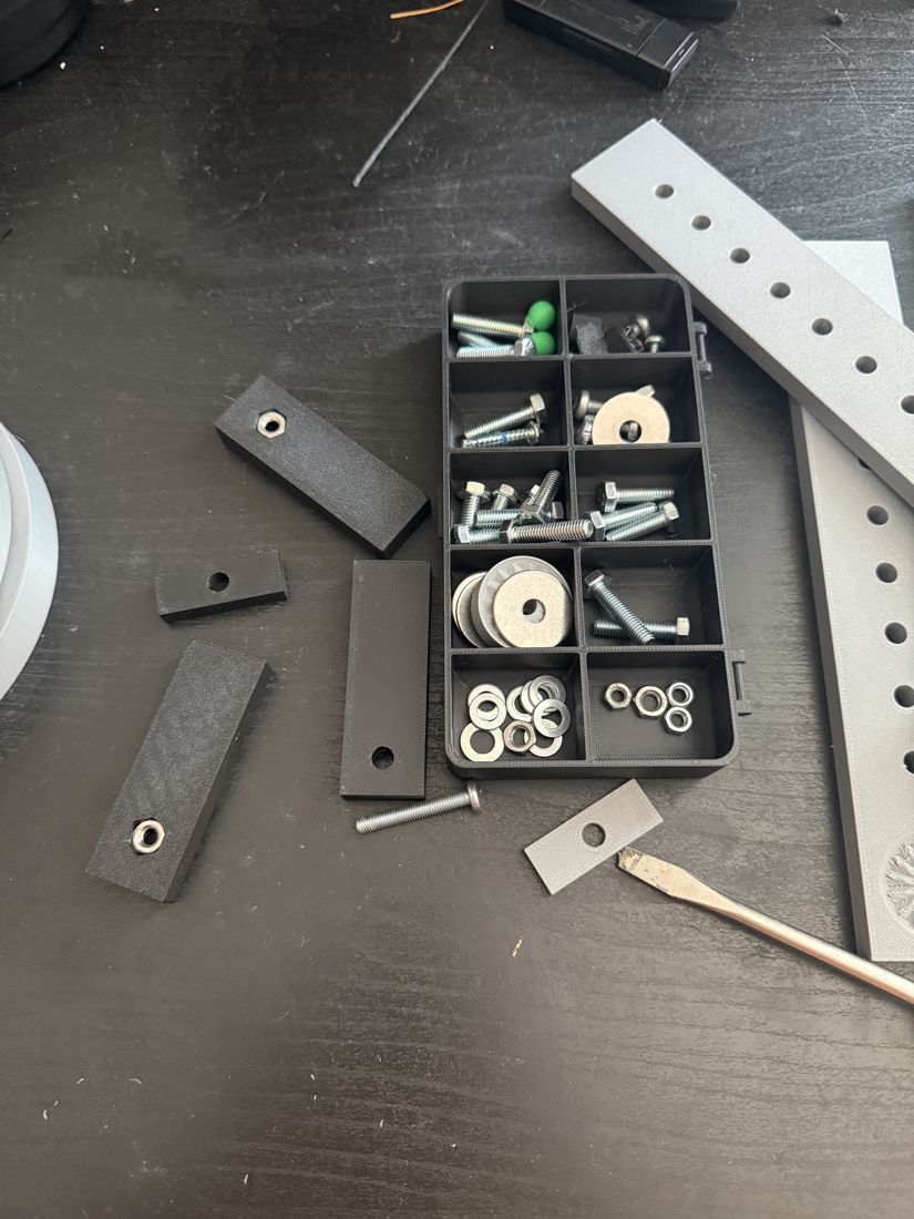 Sorted hardware bin with screws, washers, nuts, and printed arm pieces, used across all iterations